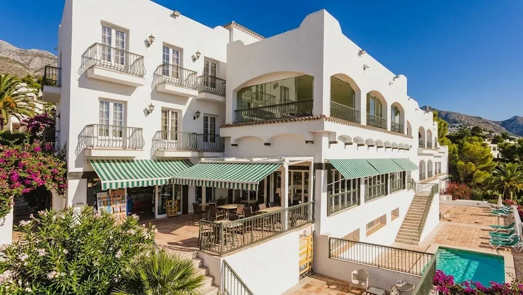Белый фасад здания Altea Club de Golf, где находится клиника Cosmetology Lab, с террасой и бассейном